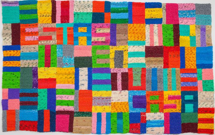 Image of a colorful geometric quilted pattern, made from crocheted plastic bags. 