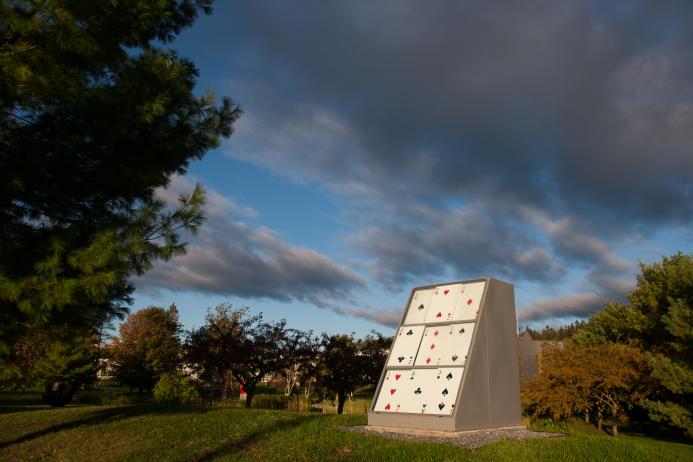 Image of Way Station I (Study Chamber) in a field. Sculpture is composed of 9 large playing cards in a gray polygonal plinth. 