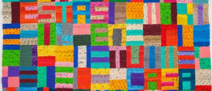 Image of a colorful geometric quilted pattern, made from crocheted plastic bags. 